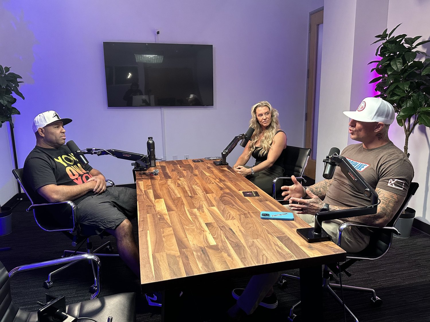 Three people around a wooden conference table with microphones